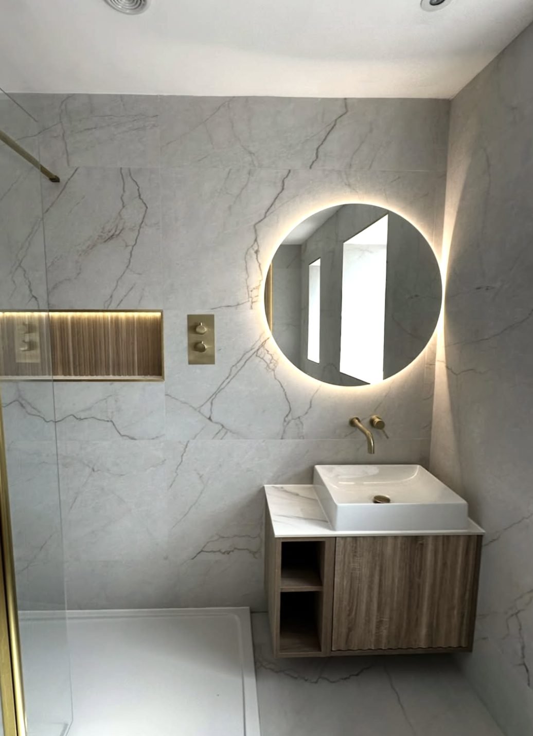 Marble effect shower room with backlit round mirror and oak vanity